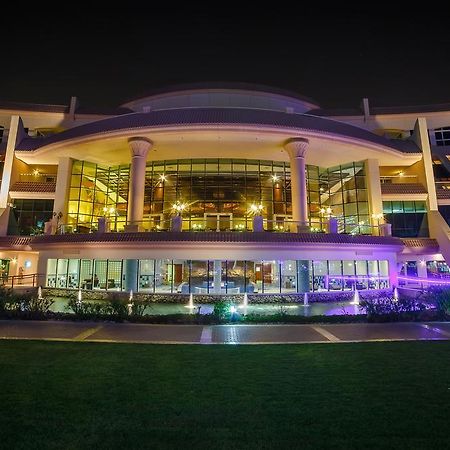 Al Raha Beach Resort & Spa Abu Dhabi Ngoại thất bức ảnh The photo shows a modern architectural building illuminated at night. The structure has a large central entrance with multiple glass windows, flanked by symmetrical columns. The exterior features a combination of sleek lines and curves, with lighting