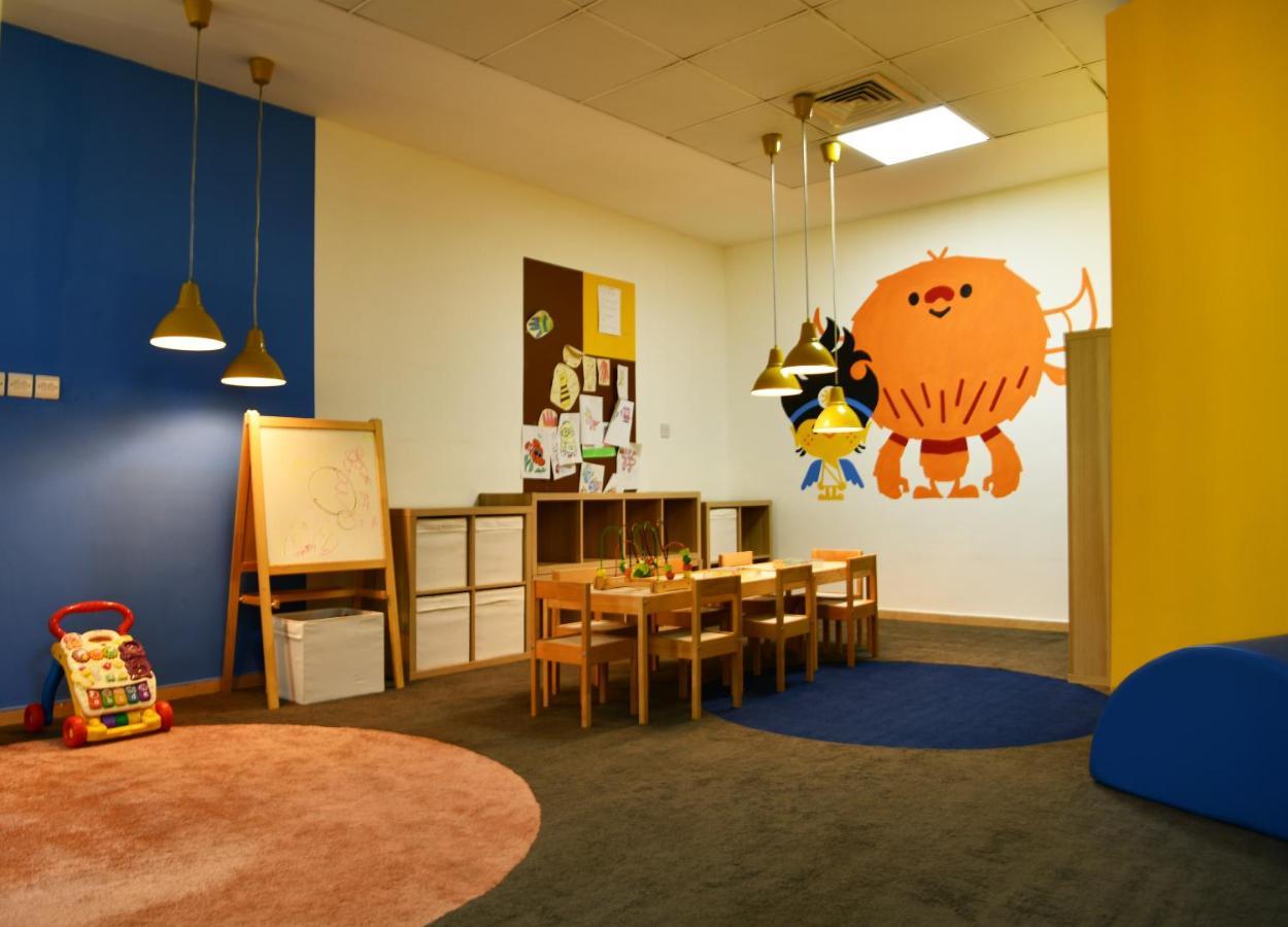 Al Raha Beach Resort & Spa Abu Dhabi Ngoại thất bức ảnh The photo shows a colorful children's classroom or play area. The walls are painted in various shades, including blue and yellow. There is a large, playful character mural on one wall that appears to be a friendly monster. 

In the room, there is a s