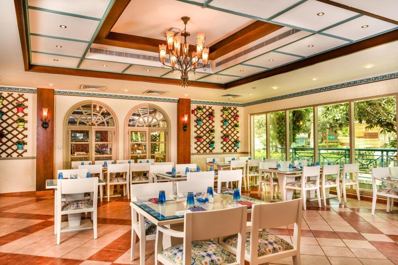 Al Raha Beach Resort & Spa Abu Dhabi Ngoại thất bức ảnh The photo shows the interior of a restaurant or dining area. The space has a warm and inviting atmosphere, featuring a mix of decorative elements. 

- **Seating**: There are several white wooden tables and chairs arranged throughout the area, some wi