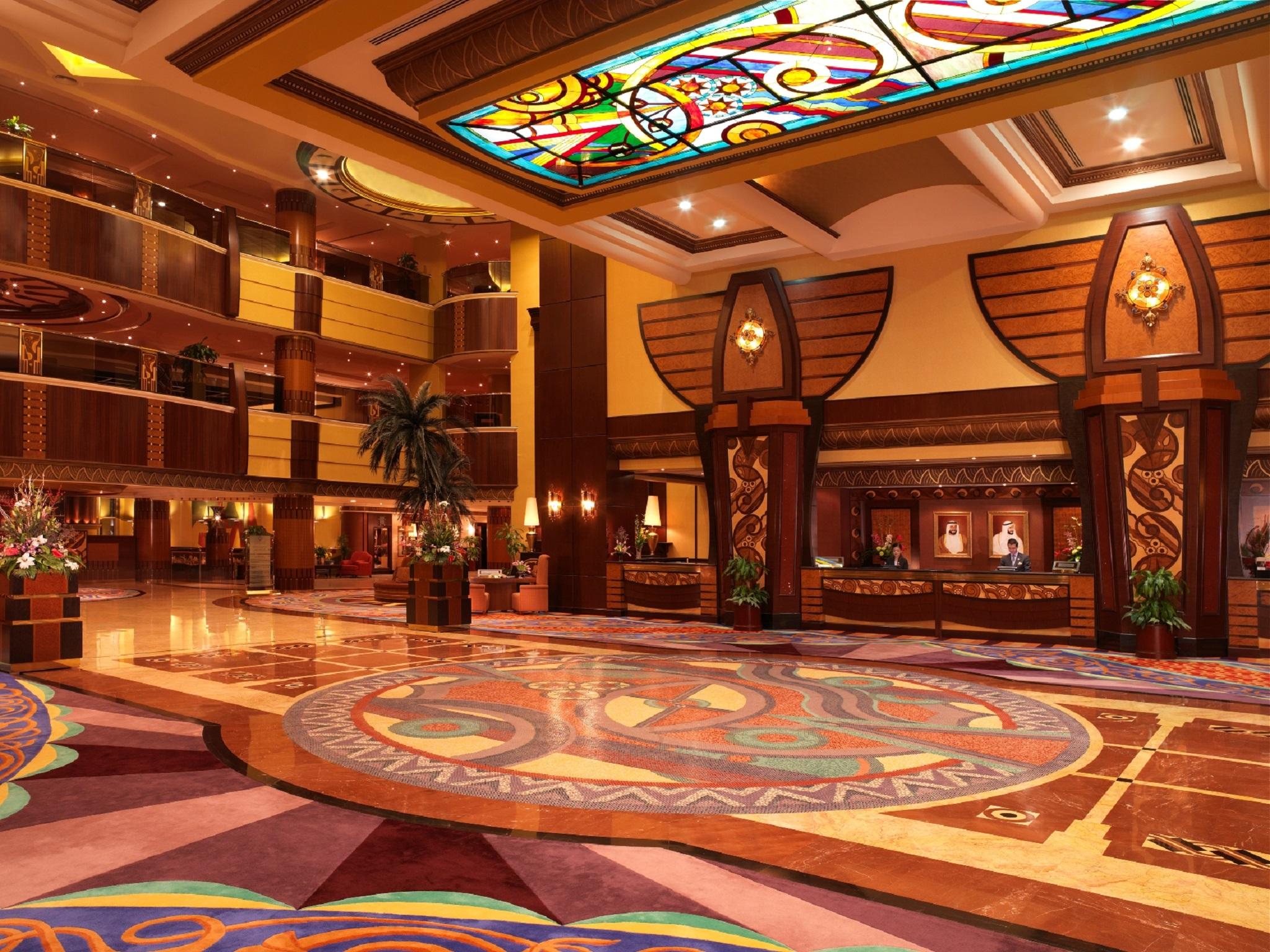 Al Raha Beach Resort & Spa Abu Dhabi Nội địa bức ảnh The photo depicts an elegantly designed hotel lobby. It features a grand ceiling with intricate stained glass and decorative patterns. The floor is adorned with colorful, ornate designs, including circular patterns. The lobby is spacious, with wooden