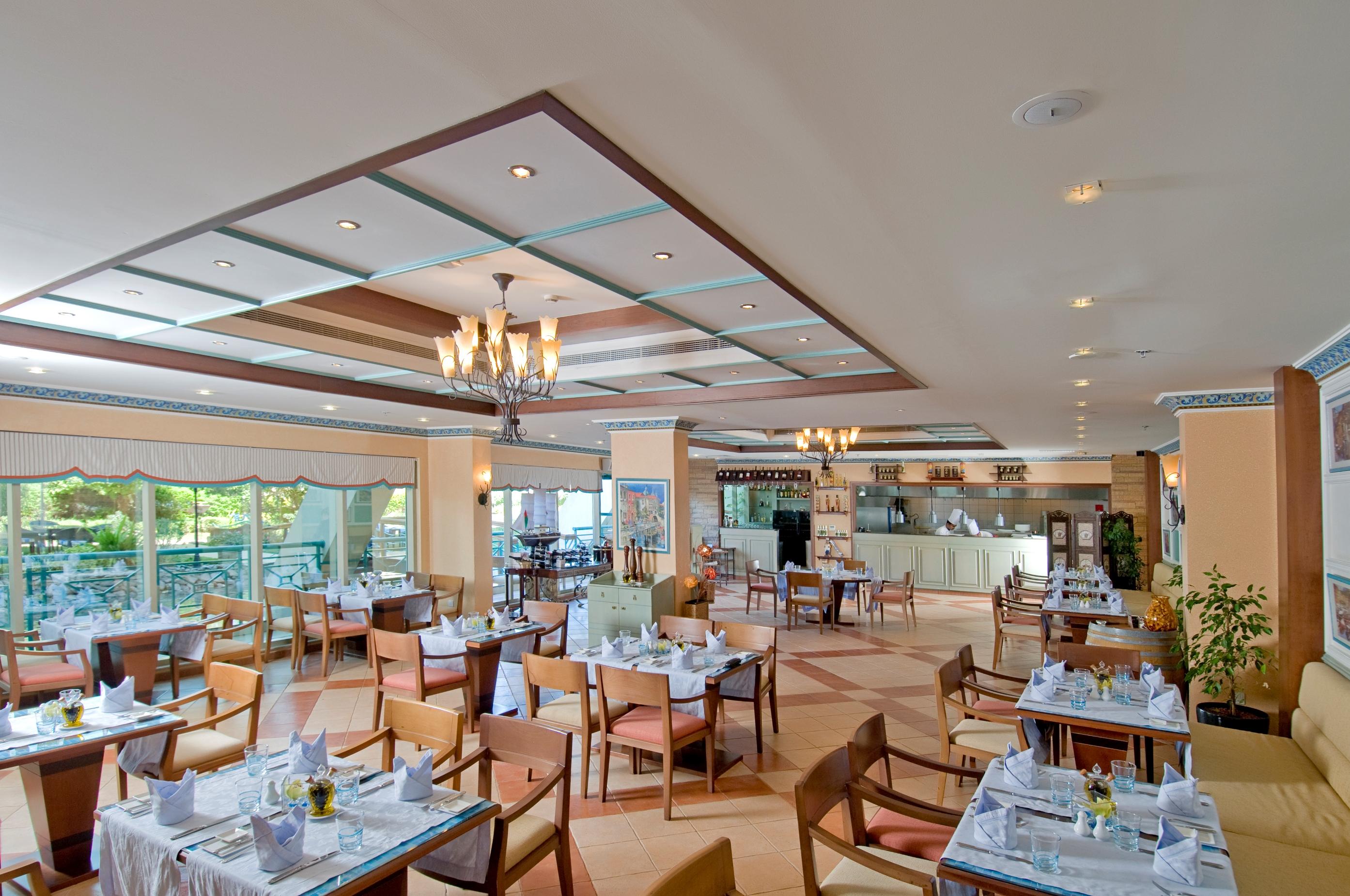 Al Raha Beach Resort & Spa Abu Dhabi Nhà hàng bức ảnh The photo shows the interior of a restaurant. It features a spacious dining area with multiple tables neatly arranged, each set with tableware and cloth napkins. The decor includes a decorative ceiling with lighting fixtures, and large windows that p