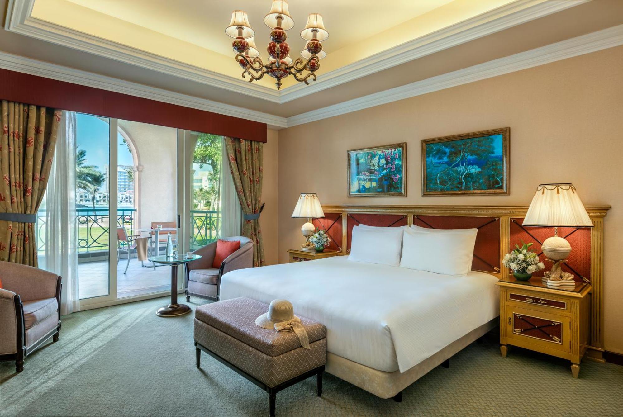 Al Raha Beach Resort & Spa Abu Dhabi Ngoại thất bức ảnh The image depicts a well-furnished hotel room. It features a large bed with white linens, flanked by two bedside lamps. Above the bed, there are two pieces of artwork hanging on the walls. To the side, there is a comfortable armchair and a small tabl