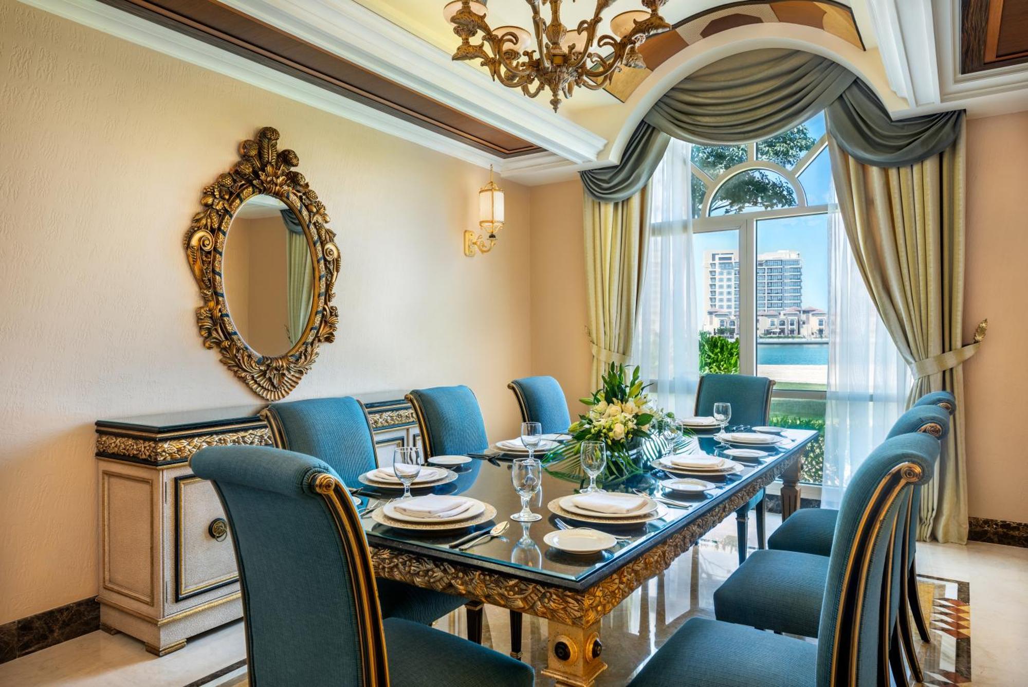Al Raha Beach Resort & Spa Abu Dhabi Ngoại thất bức ảnh The photo features an elegantly decorated dining room. It includes a long, polished table set for a meal with plates, glasses, and decorative items, surrounded by plush blue chairs. The room is adorned with sophisticated details, such as an ornate mi