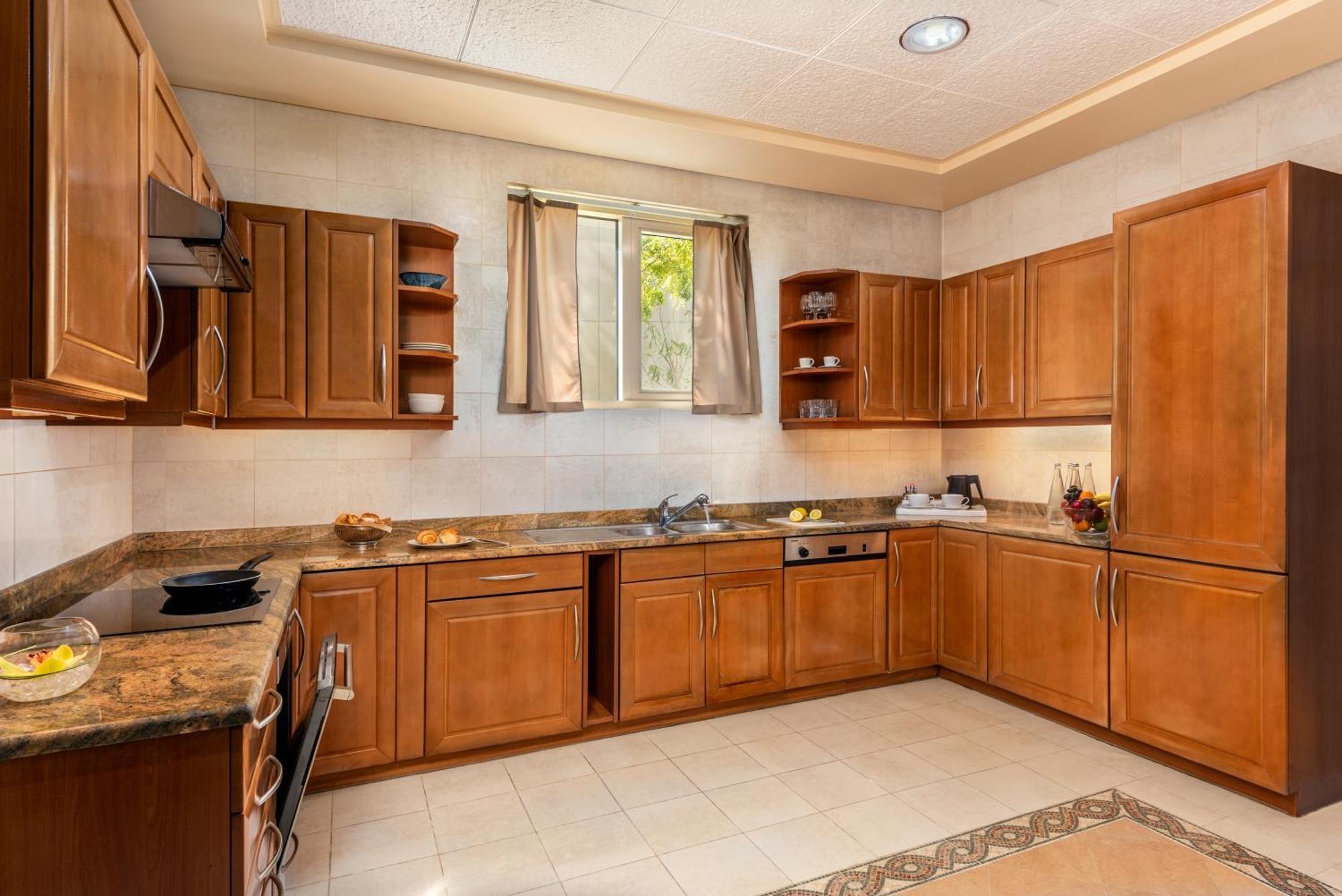 Al Raha Beach Resort & Spa Abu Dhabi Ngoại thất bức ảnh The photo shows a cozy kitchen featuring wooden cabinets with a rich brown finish, providing a warm and inviting atmosphere. The countertops are made of a light-colored stone, complementing the cabinetry. There is a window above the sink, allowing na
