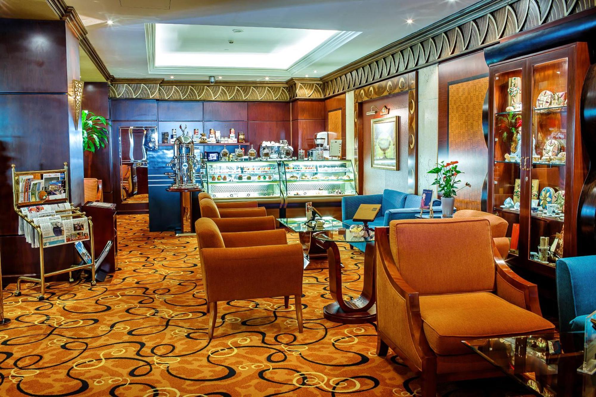 Al Raha Beach Resort & Spa Abu Dhabi Ngoại thất bức ảnh The photo shows a cozy and elegantly designed lounge or café area. It features plush seating with brown armchairs and a blue couch. In the background, there is a display case filled with various items, likely including pastries or decorative goods. T