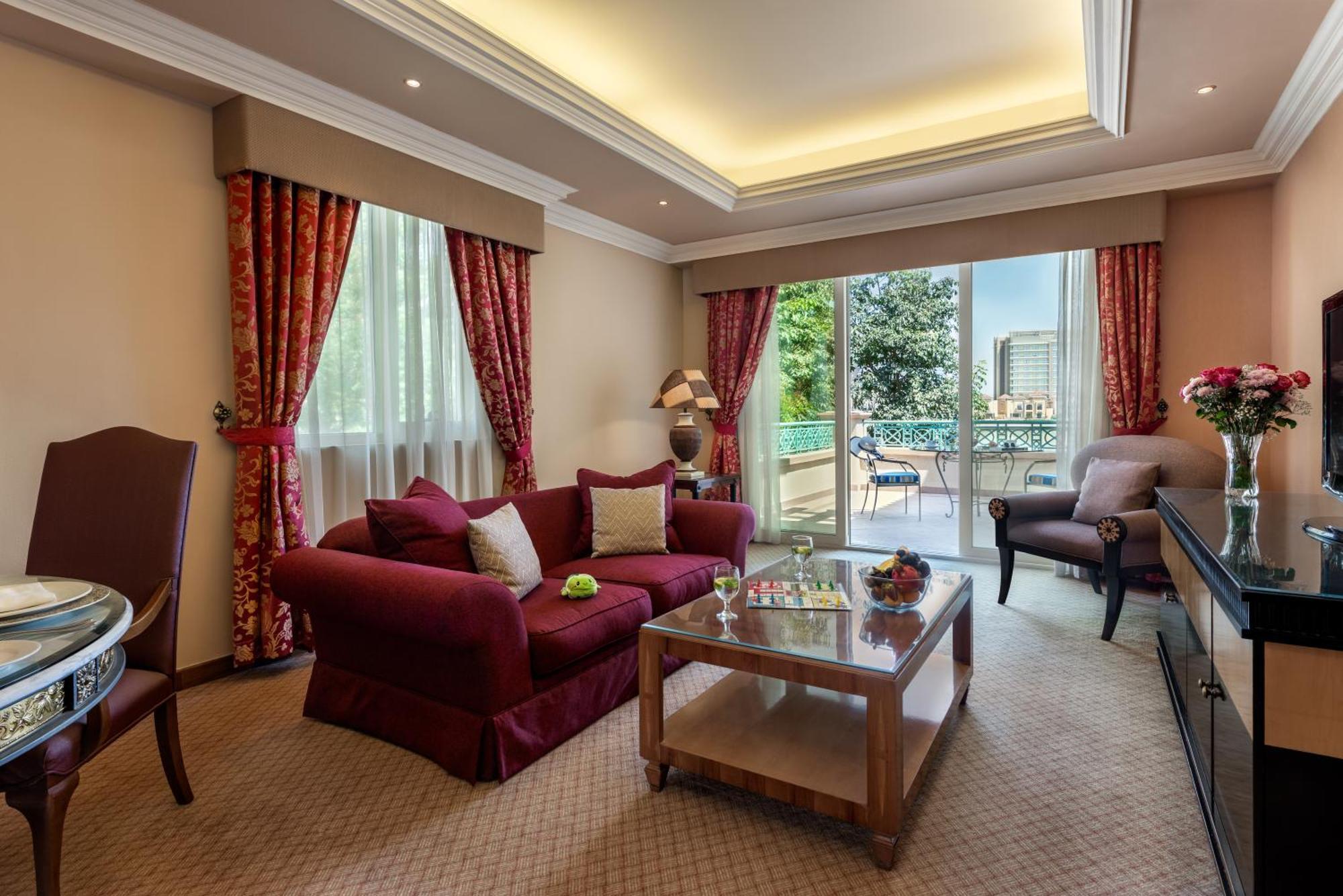 Al Raha Beach Resort & Spa Abu Dhabi Ngoại thất bức ảnh The photo shows a well-decorated hotel room or living area. It features a cozy seating arrangement with a deep red couch adorned with cushions, paired with a single chair. There is a glass coffee table in front of the couch, which is set on a plush c