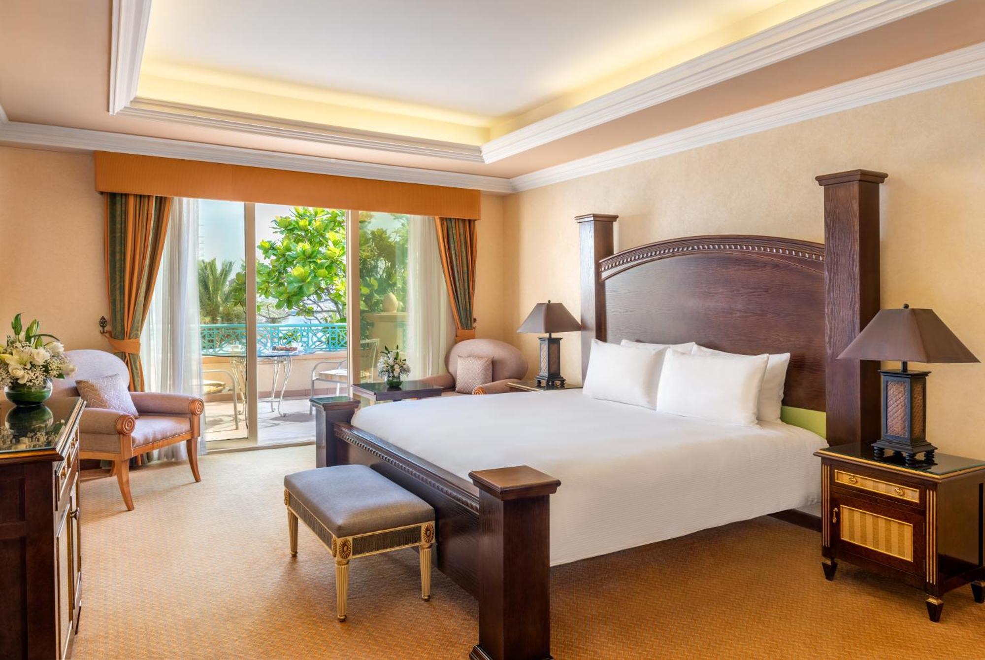 Al Raha Beach Resort & Spa Abu Dhabi Ngoại thất bức ảnh The photo shows a well-appointed hotel bedroom. It features a large bed with white bedding, flanked by bedside tables with lamps. The room has light-colored walls and a warm-toned carpet. There is a comfortable seating area with a chair and a small t