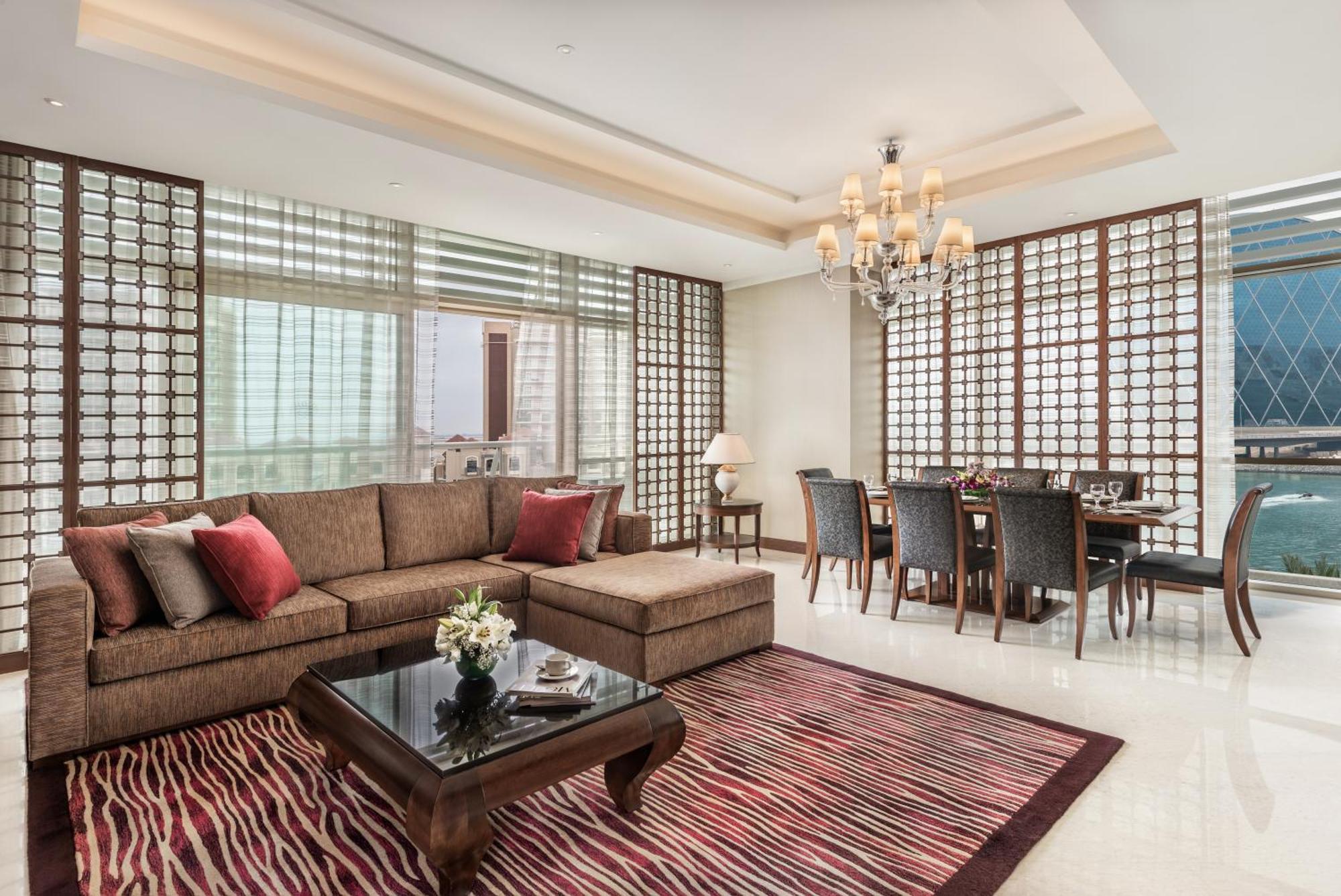 Al Raha Beach Resort & Spa Abu Dhabi Ngoại thất bức ảnh The photo shows a stylish and modern living space. On one side, there is a comfortable sectional sofa in a brown upholstery, accented with red and gray cushions. In front of the sofa, there is a glossy black coffee table adorned with a small floral a