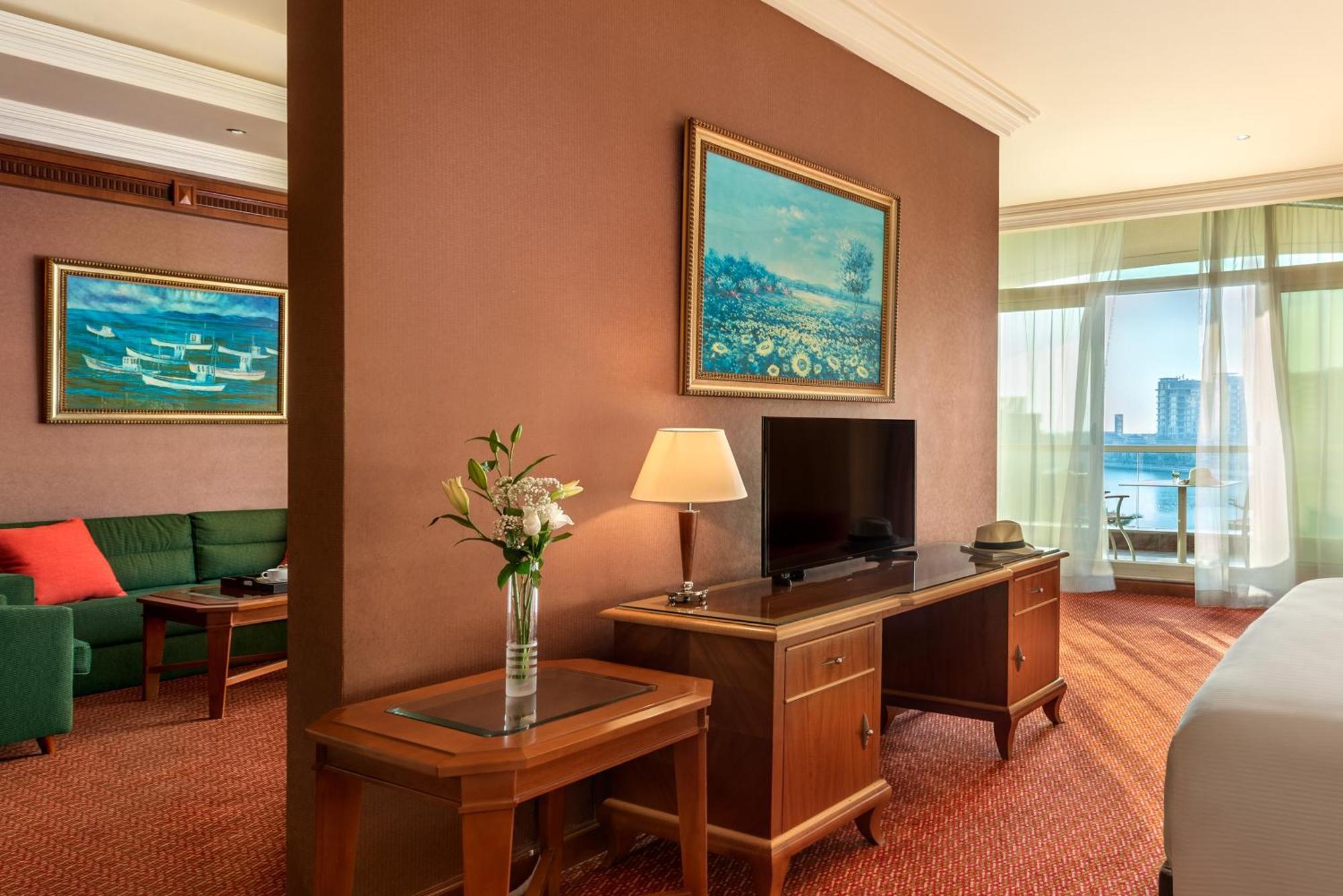 Al Raha Beach Resort & Spa Abu Dhabi Phòng bức ảnh The photo shows a hotel room with a warm, inviting atmosphere. There's a large window that provides natural light and a view, likely overlooking a cityscape or water. On one wall, there's a piece of artwork featuring a landscape, and nearby, a small 