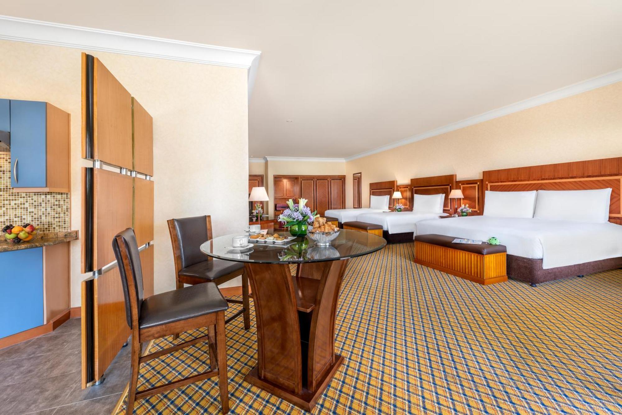 Al Raha Beach Resort & Spa Abu Dhabi Phòng bức ảnh The photo displays a spacious hotel room. It features two large beds with white bedding, a circular glass dining table with a decorative floral centerpiece, and a couple of chairs around it. There is a wooden cabinet along one wall, and the room has 
