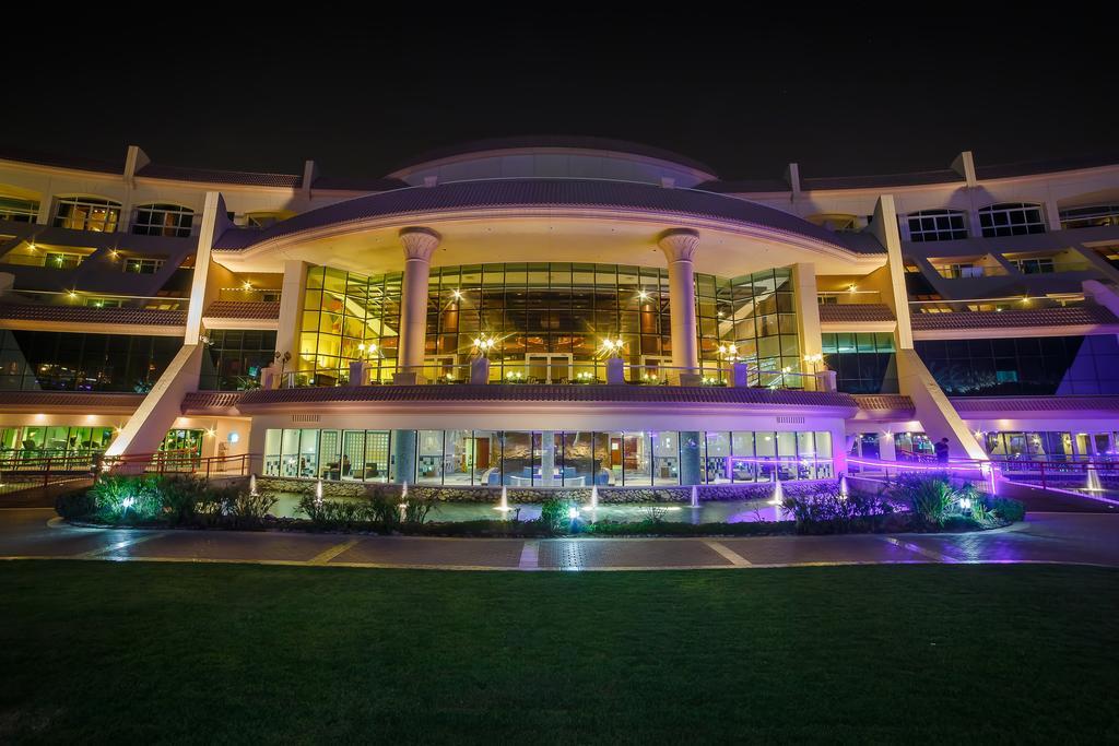 Al Raha Beach Resort & Spa Abu Dhabi Ngoại thất bức ảnh The photo shows a modern architectural building illuminated at night. The structure has a large central entrance with multiple glass windows, flanked by symmetrical columns. The exterior features a combination of sleek lines and curves, with lighting